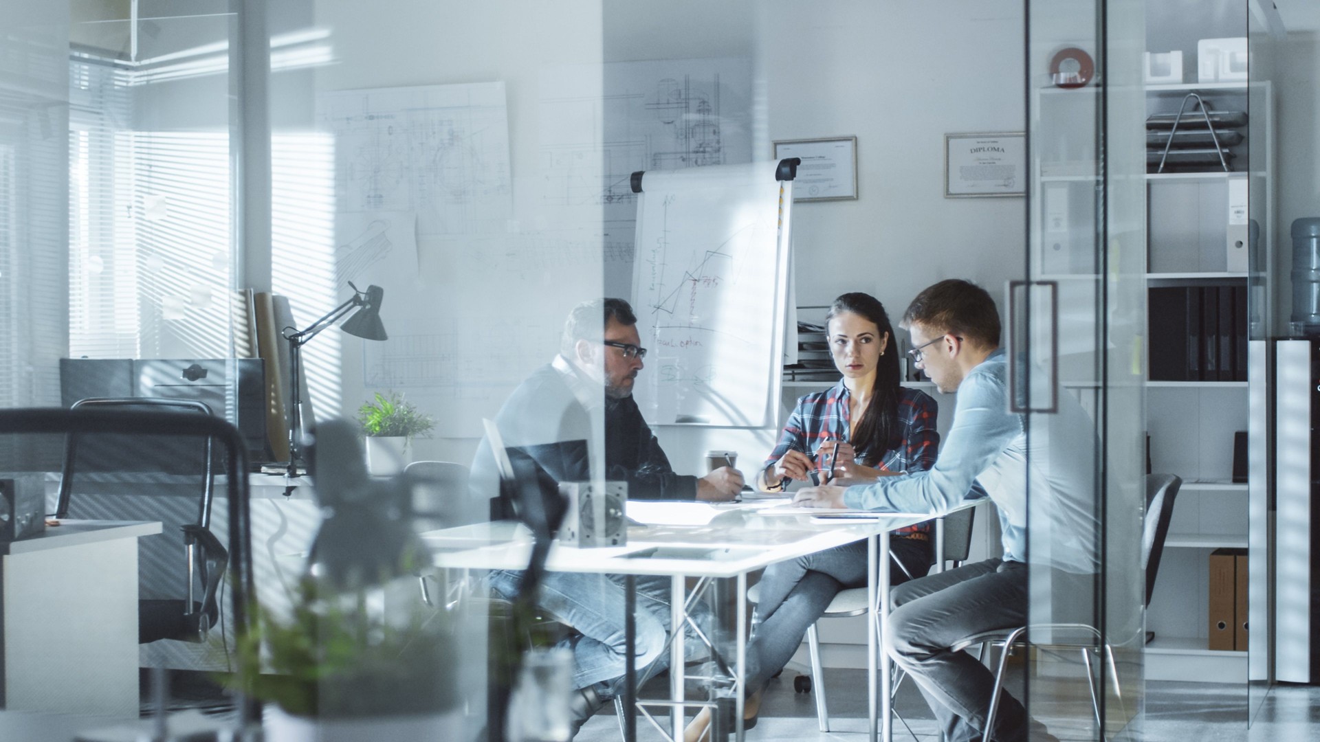 Morning Meeting of Design Engineers. Exchange of Ideas and Plans is Happening. In the Background Whiteboard with Diagrams, Blueprints on the Wall.